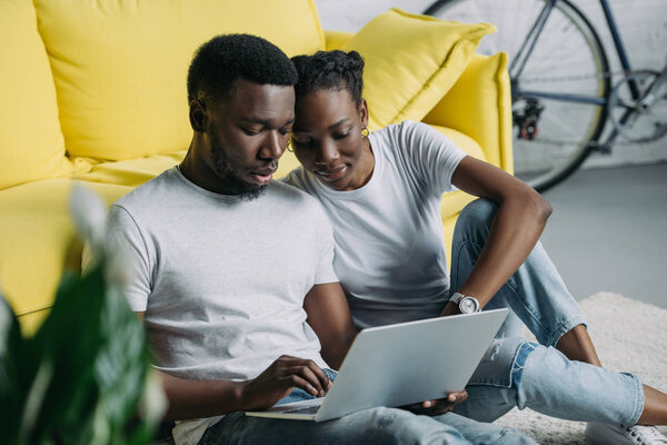 young african american couple in white t-shirts using laptop together at home