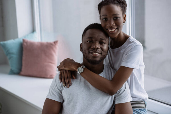 happy young african american couple in white t-shirts smiling at camera at home 