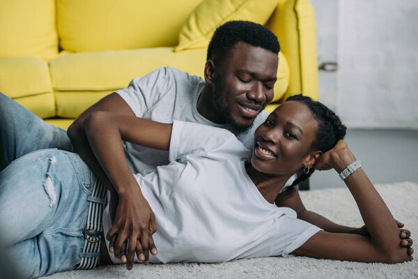 happy young african american couple lying on carpet together at home