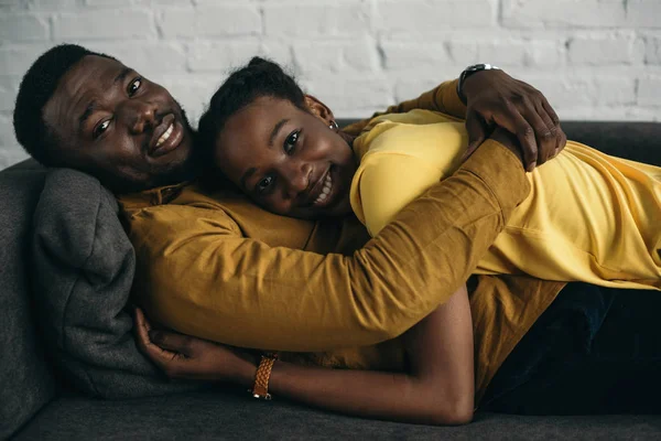 快乐的年轻非洲裔美国人夫妇在黄色衬衫躺在一起在沙发上 微笑着在相机 — 图库照片