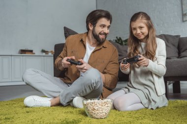 Baba ve halı üzerinde oturan ve video oyunu oynayan kız