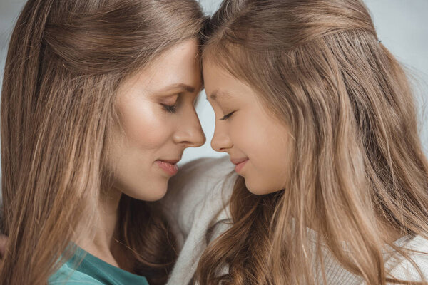 side view of mother and daughter touching with foreheads at home