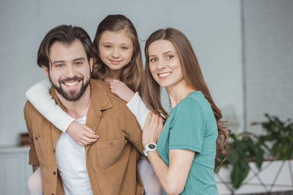 happy parents and daughter looking at camera at home 