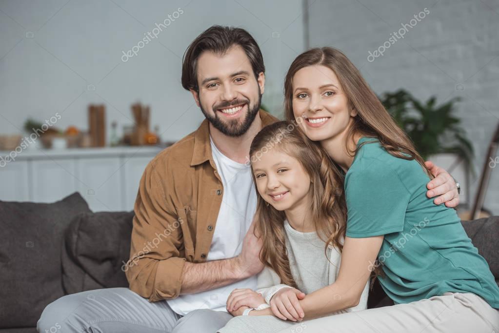 Happy parents and daughter looking at camera at home