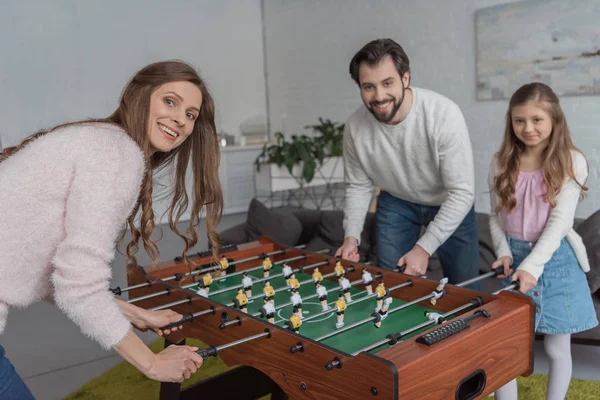 parents and daughter playing table soccer at home