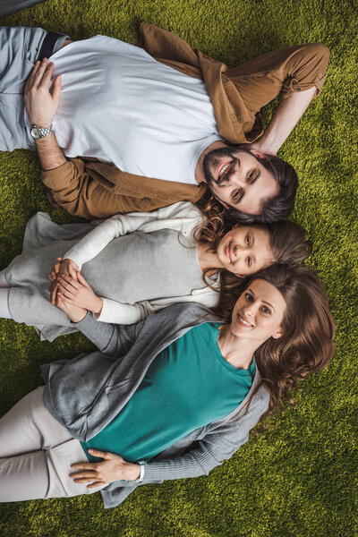 top view of family lying on green carpet and looking at camera