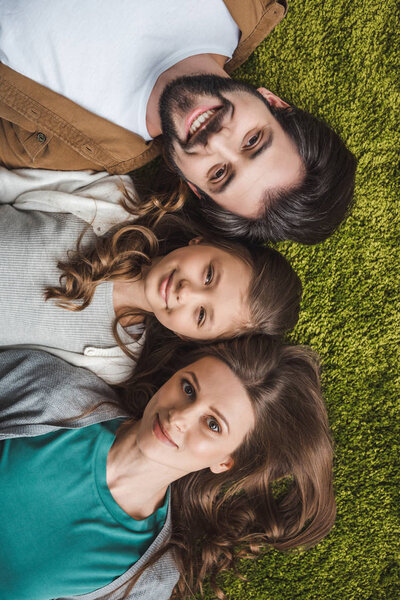 top view of parents and daughter lying on green carpet and looking at camera