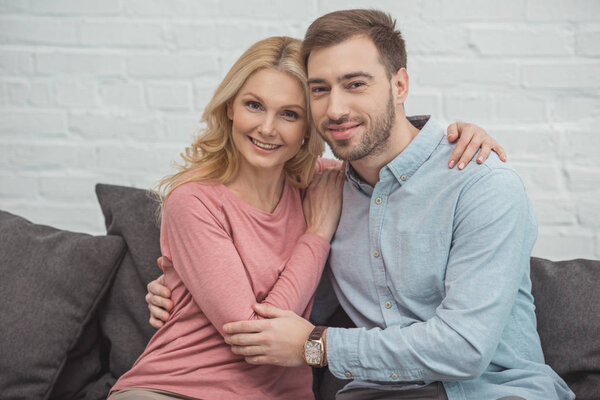 portrait of smiling mother and grown son hugging each other while sitting on sofa
