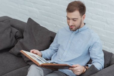 evde koltukta istirahat ederken fotoğraf albümündeki fotoğrafları bakarak adam portresi