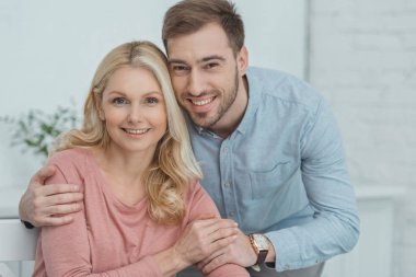 gülümseyen yetişkin oğlu anne sarılma ve evde kameraya bakarak portresi