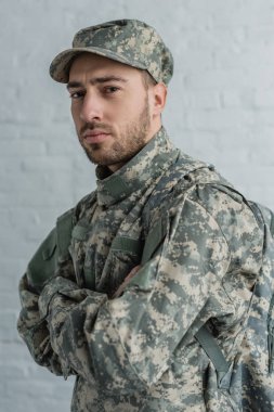 portrait of soldier in military uniform looking at camera against white brick wall clipart
