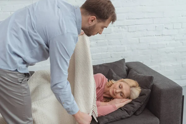 Vorsichtiger Erwachsener Sohn Deckt Schlafende Mutter Auf Sofa Mit Decke — kostenloses Stockfoto