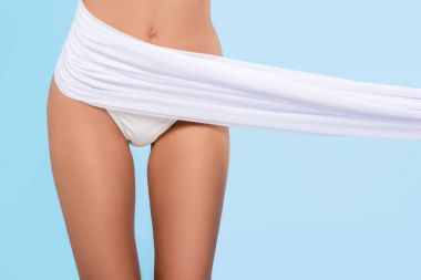 cropped view of tanned slim girl in bikini posing with white veil, isolated on blue clipart