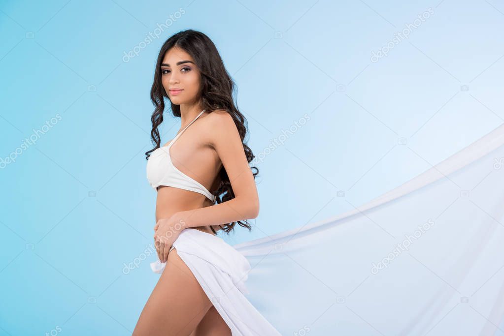 beautiful young woman in bikini posing with white veil, isolated on blue