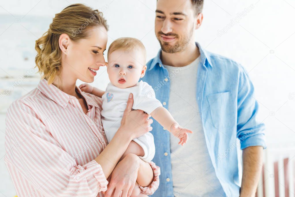 Mother holding infant daughter while father standing near 