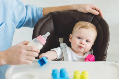 Holding besleme şişe ve plastik bloklarla bebek sandalyede oturan bebek kızı babası görünümünü kırpılmış