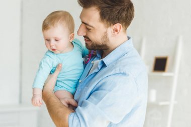 Gülümseyen baba bebek kızı elinde tutan