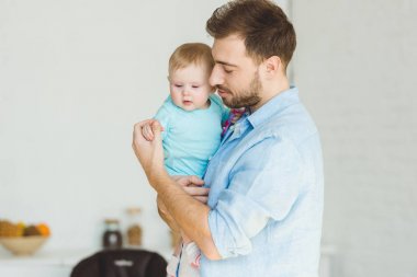 Bebek kızı basılı tutup elini dokunmadan gülümseyen genç Baba