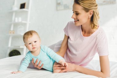 Gülümseyen anne bebek kızı yatakta holding