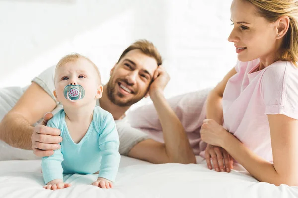両親とベッドでダミーの赤ちゃんと幼い娘の笑顔 — ストック写真