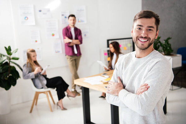 selective focus of smiling marketing manager looking at camera with multicultural colleagues behind in office