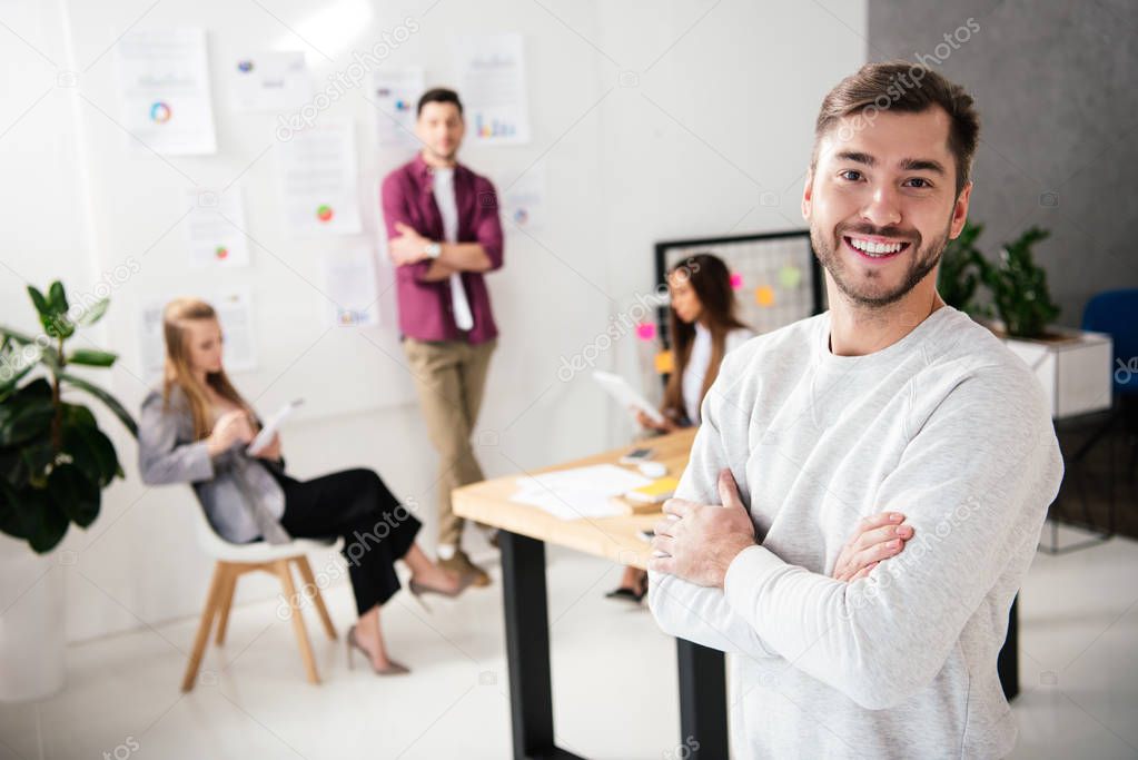 selective focus of smiling marketing manager looking at camera with multicultural colleagues behind in office