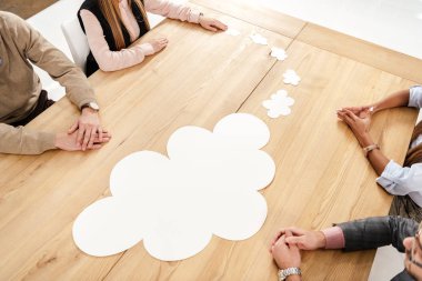 partial view of multiracial business people at wooden table with empty paper clouds, teamwork concept clipart