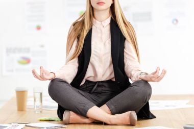 cropped shot of businesswoman meditating in lotus position on table in office clipart