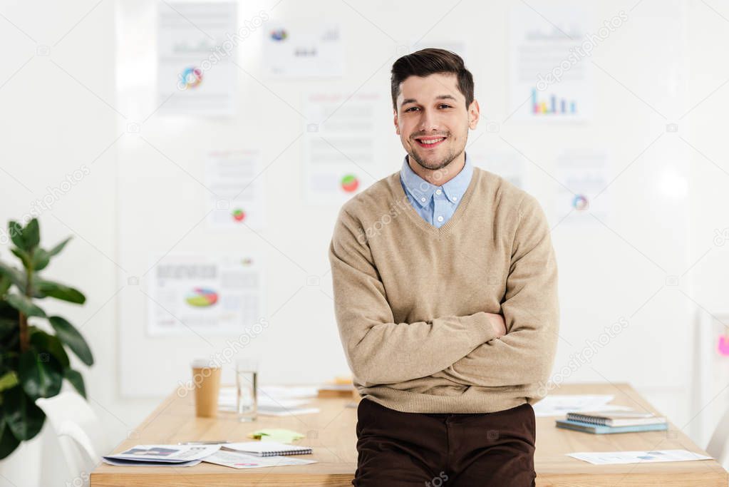 portrait of smiling marketing manager with arms crossed leaning on workplace in office