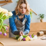 Young florist working with beautiful tulip flowers at workplace