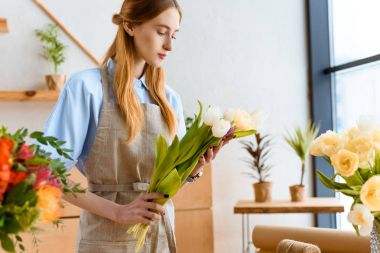 young florist in apron holding beautiful tulips in flower shop clipart