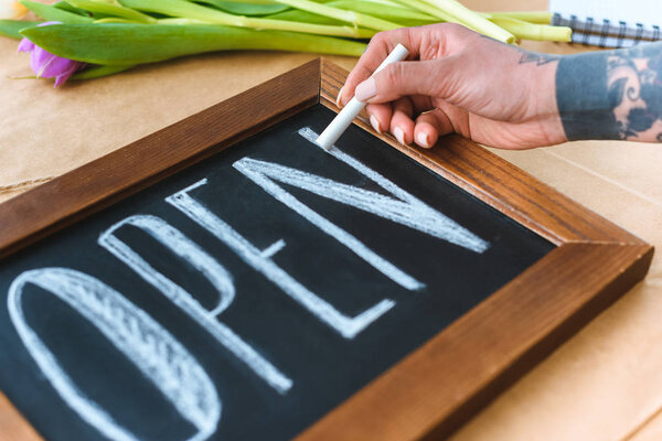 close-up partial view of young florist writing word open on board