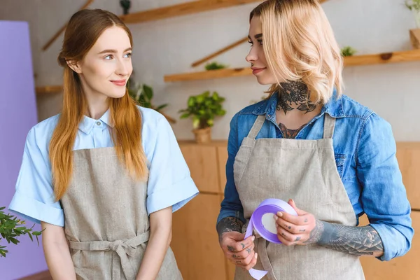 Stock image beautiful young florists in aprons smiling each other at workplace