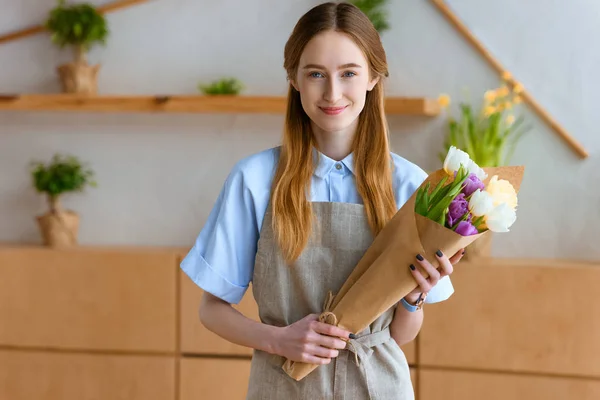 美丽的年轻花店持有郁金香和微笑在相机的花束 — 图库照片