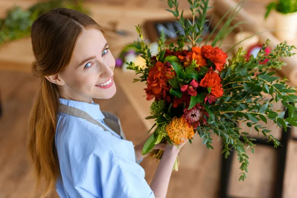 美丽的年轻花店的高角度观看鲜花和微笑的相机 — 图库照片