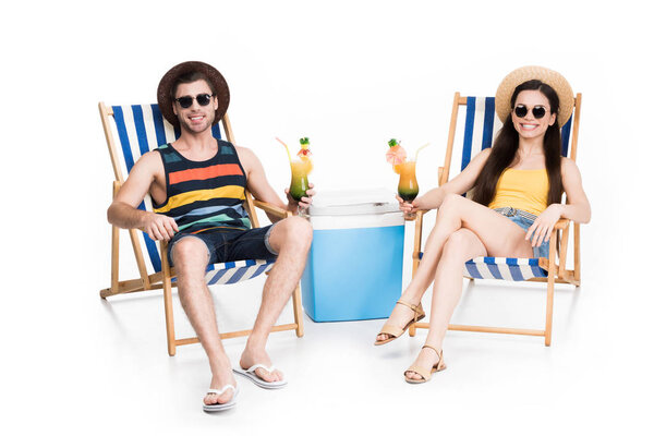 smiling couple relaxing on beach chairs with cocktails and cooler box, isolated on white
