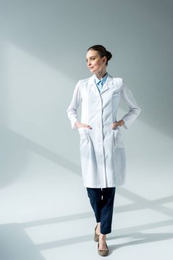 serious female doctor in white coat looking away on grey clipart