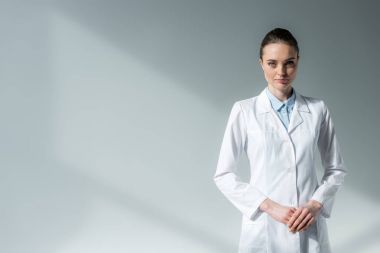 beyaz ceket gri kameraya bakarak ciddi kadın doktor