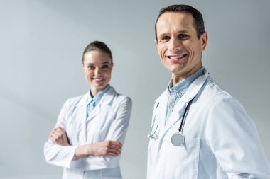 happy adult doctors looking at camera isolated on grey