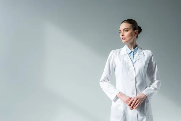 Ελκυστική Γυναίκα Γιατρό Λευκό Παλτό Κοιτάζοντας Μακριά Γκρι — Φωτογραφία Αρχείου