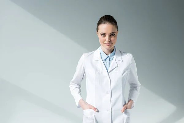 Sorridente Médico Feminino Casaco Branco Olhando Para Câmera Cinza — Fotografia de Stock
