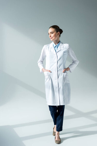 serious female doctor in white coat looking away on grey