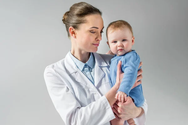 Sorridente Pediatra Femminile Che Tiene Bambino Piccolo Sul Grigio — Foto Stock