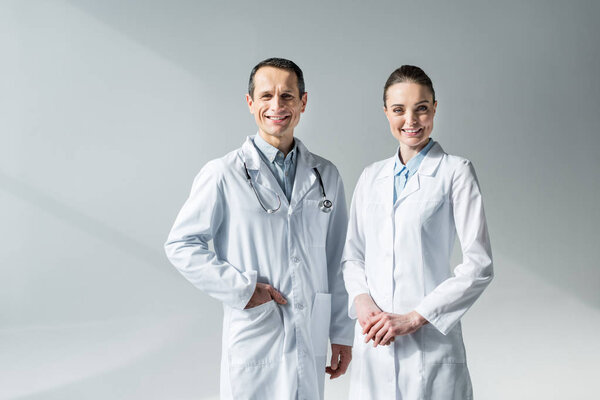 smiling adult doctors looking at camera on grey