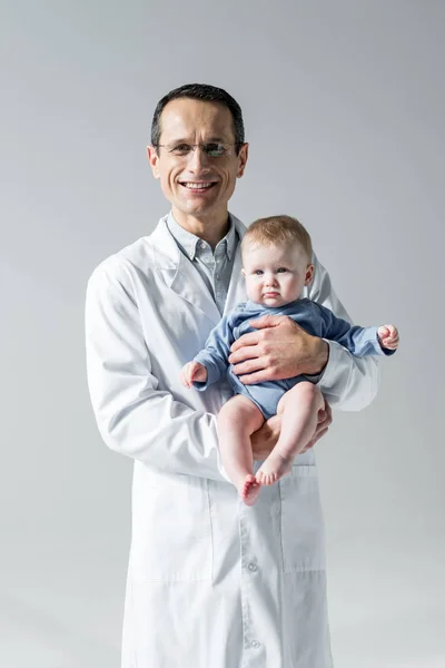 小さな赤ちゃんを押しながらグレーの分離カメラ目線笑顔の大人の小児科医 — ストック写真