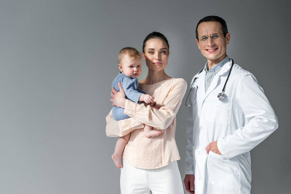mother and child looking at camera with pediatrician on grey