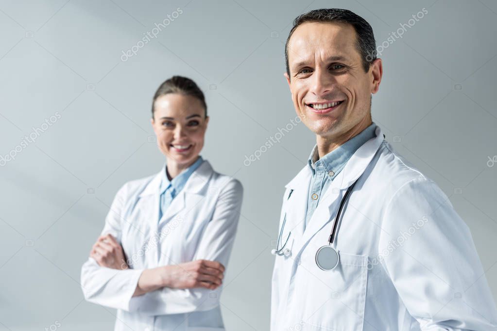 happy adult doctors looking at camera isolated on grey