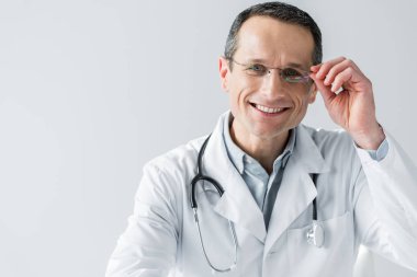 İşyerinde oturan ve üzerinde beyaz izole kamera bakarak mutlu yetişkin doktor