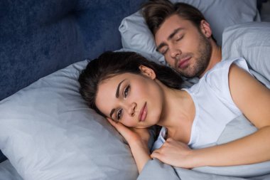 Smiling woman lying by her sleeping husband in bed clipart