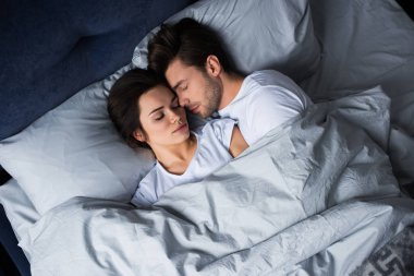 Bearded man embracing attractive brunette woman while sleeping in bed clipart